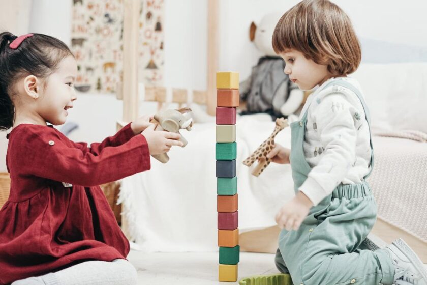 Two young children sitting on the floor building a tall tower of colorful wooden blocks together