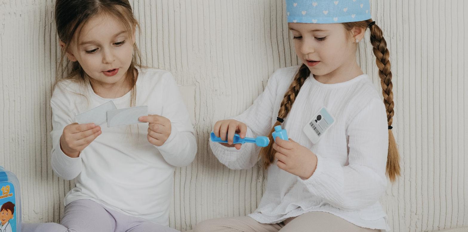Two young children sitting side by side, absorbed in pretend play with a toy doctor kit